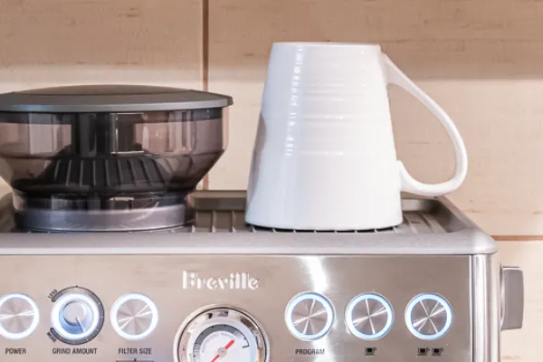 Breville Barista Express BES870 em bancada doméstica com xícara pré-aquecida na bandeja superior e painel de controles iluminado